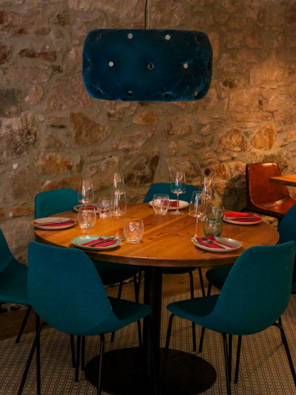 Mesa redonda con sillas turquesa bajo lámpara de terciopelo en pared de piedra